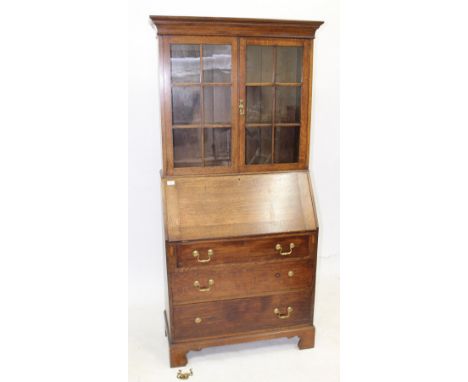 AN EARLY 20TH CENTURY JAS SHOOLBRED OAK BUREAU BOOKCASE with twin glazed doors above fall front opening to reveal pigeon hole