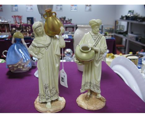 A Pair of Royal Worcester Figures of Cairo Water Carriers, each holding a large urn, their cream robes with black foliate dec