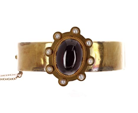 Antique yellow metal garnet an seed pearl hinged bangle, mounted with a large oval garnet cabouchon in a border of eight pear