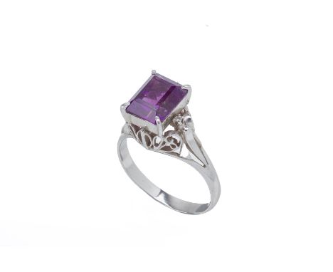 AN AMETHYST AND DIAMOND RING
Set in platinum, the emerald cut amethyst with a singular round brilliant cut diamond to each sh