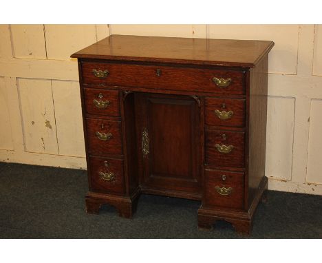 A George III oak kneehole desk, with rectangular top above an arrangement of seven drawers, and central cupboard, on bracket 