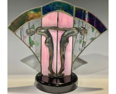 An Art Deco style table lamp, cast with a pair of nude dancing girls in profile before a fan shaped stained glass panel shade