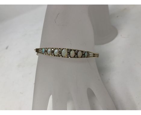 A 9ct gold, opal and diamond bangle set with seven opals flanked by 14 diamonds. Approximate weight 15.3 grams. In original b