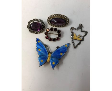 An assortment of silver brooches including an enamel brooch in the form of a butterfly and a yellow precious metal brooch.