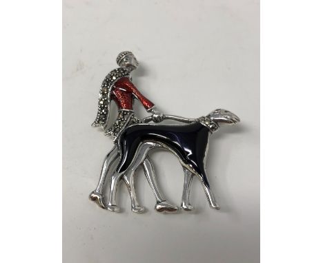 A silver and enamel brooch in the form of an Art Deco styled lady walking a dog.