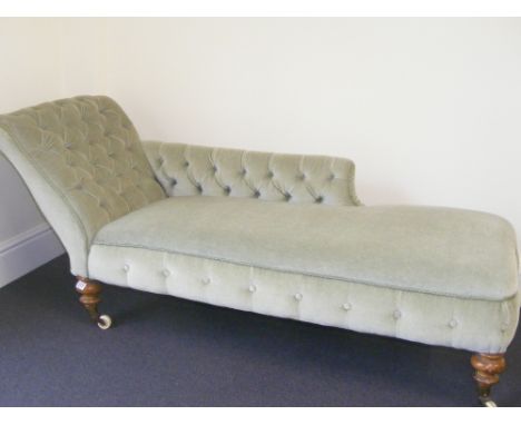 A Victorian upholstered button back chaise longue, raised on turned supports terminating in brass cups to porcelain castors.