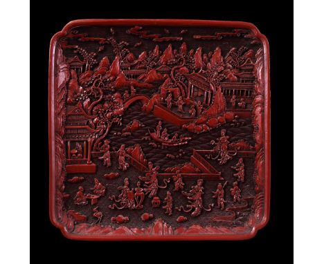 Cinnabar plaque with richly carved decoration of many figures in a landscape with pagodas and boat on a river, in the lower e