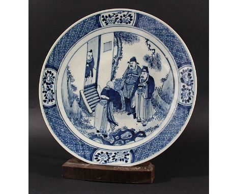 CHINESE BLUE AND WHITE CHARGER, painted with three figures outside a house, inside a trellis and cartouche border, Kangxi sty