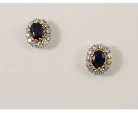 A PAIR OF SAPPHIRE AND DIAMOND CLUSTER STUD EARRINGS each set with an oval-shaped sapphire within a surround of twelve circul