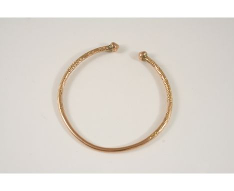 A 9CT. GOLD BANGLE with domed terminals and engraved decoration, 21 grams.