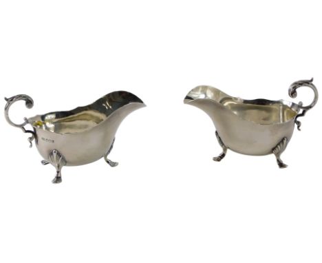 A pair of George V silver sauce boats, each with a leaf and scroll cast handle, and four cabriole legs, headed by shells, She