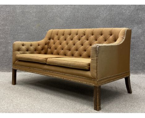 An early 20th century two seater sofa having a square button back and shaped arms over a cushioned seat upholstered in a must