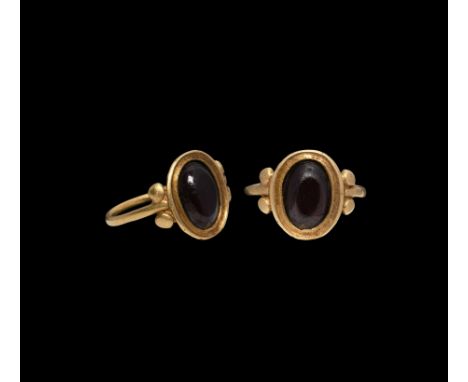 4th century AD. A gold ring with round-section hoop and oval bezel flanked by four flat 'beads', set with a garnet cabochon. 