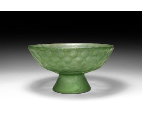 4th-6th century AD. A green glass bowl with flared foot, rounded rim and sidewall bands of facetting. Cf. Whitehouse, D., Sas