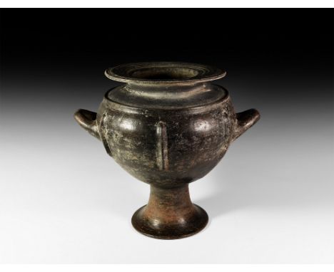 Mid 7th century BC. A dark brown ceramic vessel with high trumpet foot, globular body, large flat overhanging ribbed rim, dis