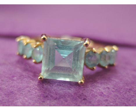 A lady's dress ring having a princess cut blue topaz style stone with set shoulders on a 9ct gold loop,  size N