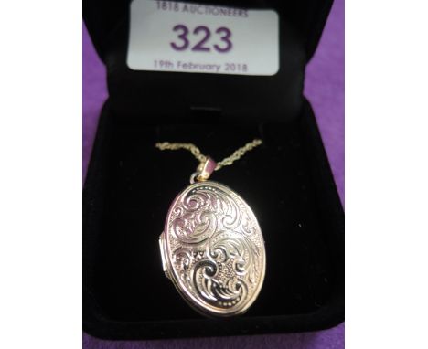 A yellow metal oval locket and chain stamped 9K having scroll decoration