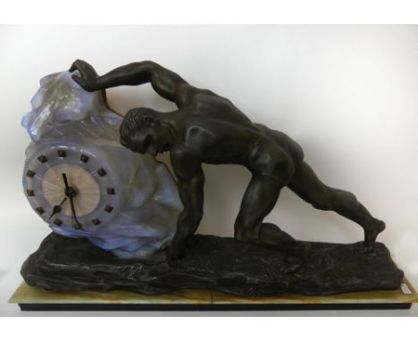 An Art Deco spelter figural clock Modelled in the form of a male figure pushing an opalescent rock which is a clock face, rai