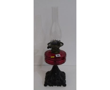 LATE VICTORIAN OIL LAMP, with cast iron foliate decorated base and red glass reservoir, 57cm including chimney 