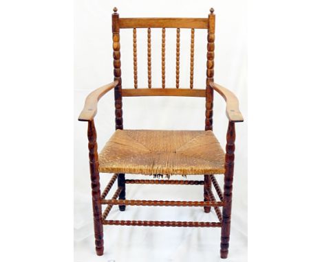 Ernest Gimson yew rush-seated armchair made by Edward Gardiner with two pointed finials to the bobbin uprights, having bobbin