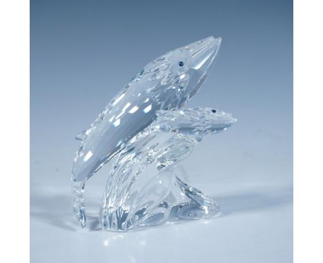 A clear faceted sculpture of a mother whale and her calf, both with blue eyes, riding the top of a wave. 1992 Swarovski Colle