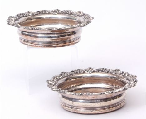 Pair of silver on copper bottle coasters each of compressed circular form with applied foliate borders and ring turned treen 