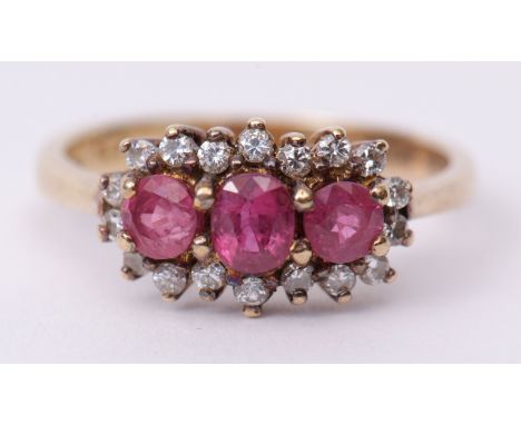 Precious metal ruby and diamond cluster ring, the 3 graduated rubies claw set and raised within a surround of 18 small diamon