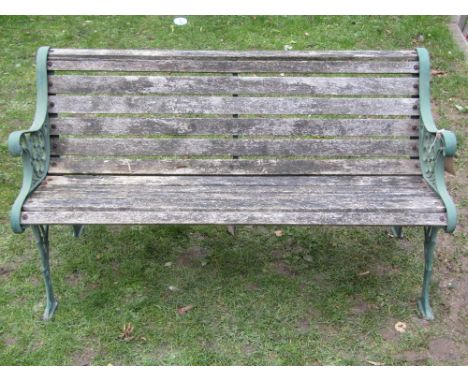 A three seat garden bench with weathered timber lathes, raised on a pair of green painted cast iron end supports with foliate