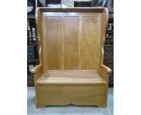 A light wood settle with winged chamfered panelled back over a hinged box seat and arms, 110 cm wide x 153 cm high