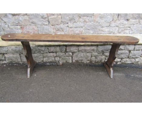 A Georgian oak bench or form, the cigar shaped top raised on a pair of shaped supports 170cm long