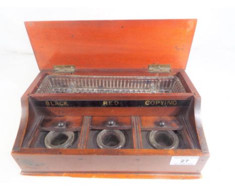 A mahogany inkwell desk set, with three glass inkwells with bun handled sliding covers and marked Black, Red, Copying, with h