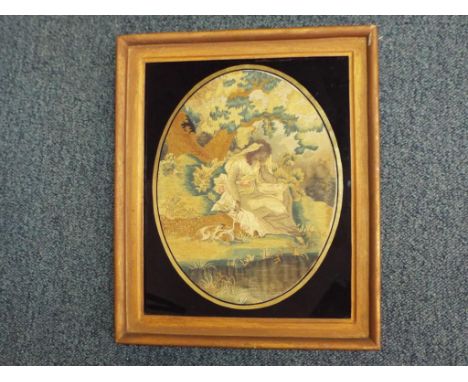A Regency printed silk and needlework oval picture depicting a woman dressed in finery seated by a tree with dog to her side,
