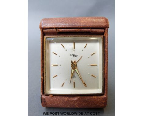 A Swiss 8 day leather cased travel alarm clock with square dial, baton numerals and luminous sword shaped hands, 52mm diamete