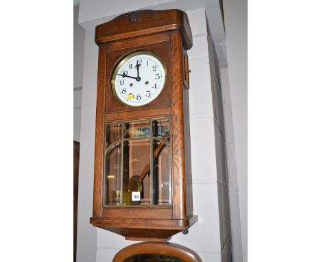 A 1930's oak wall clock with painted white face and a bevelled glass door.