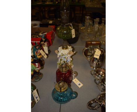 An early 20th Century oil lamp with green glass reservoir, the cast iron base decorated with herons; two other oil lamps, blu