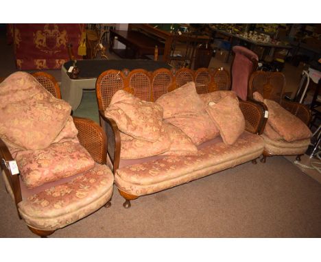 An early 20th Century bergere suite, comprising: a sofa, two matching chairs with loose cushions, raised on cabriole legs, so