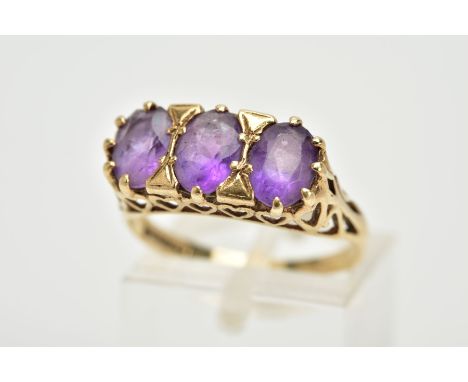 A 9CT GOLD THREE STONE AMETHYST RING, three claw set  oval cut amethysts, within a raised openwork heart detailed gallery, ha