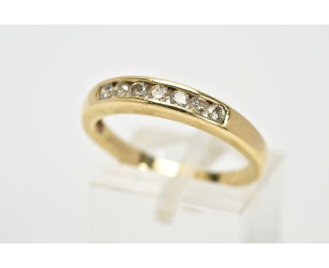 A YELLOW METAL DIAMOND HALF ETERNITY RING, designed with a row of channel set round brilliant cut diamonds, to a plain polish