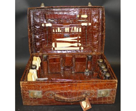 An Edwardian crocodile skin covered travelling case with fitted interior to include ivory handled brushes, shoe horns, cut th