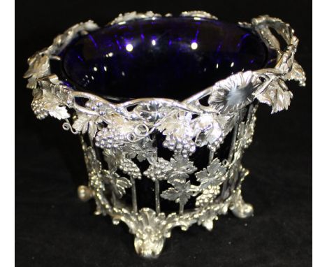 A Victorian silver swing-handled basket with grape and vine decoration, raised on four scrolling feet, with blue glass liner 