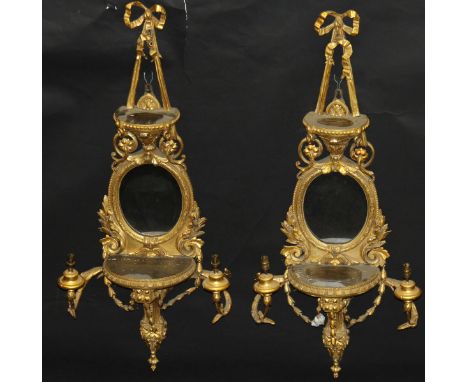 A pair of 19th Century giltwood and gesso girondole mirrors in the Rococo manner, surmounted with a bow above a shelf, oval m