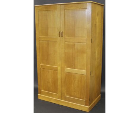 A Cotswold School oak two door wardrobe by Hugh Birkett, the simple cornice above two cupboard doors, each of three bevelled 