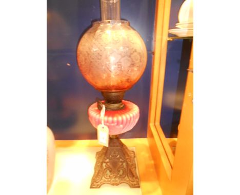 A Victorian oil lamp with floral etched shade and lobbed pink milk glass reservoir, raised on an ornate floral pierce cast ir