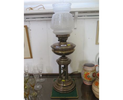 An early 20th century brass oil lamp, the moulded shade above three columns and a cherub on a moulded base, 68 cm high 