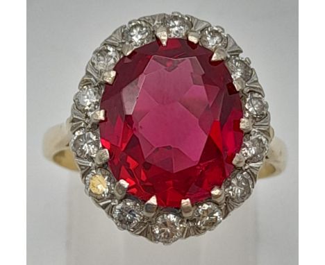 An 18K Yellow Gold Ruby and Diamond. 10ct central ruby surrounded by a halo of diamonds. Size O 1/2. 6.1g. 