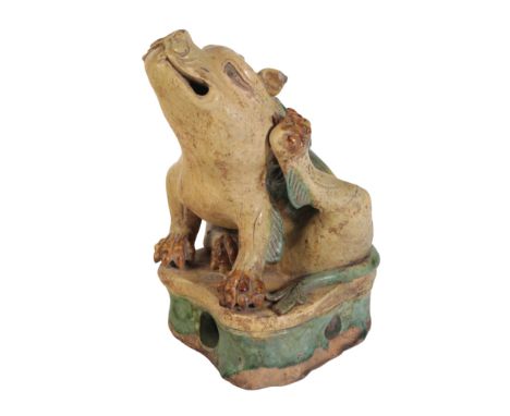 A CHINESE SANCAI POTTERY FIGURE OF A LION DOG seated and scratching its left ear, glazed in cream, green and brown, Ming, 22c
