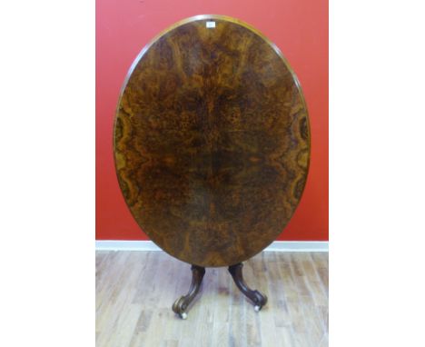 A Victorian burr walnut loo table with a moulded oval snap top raised on pedestal base and scroll work legs with ceramic cast