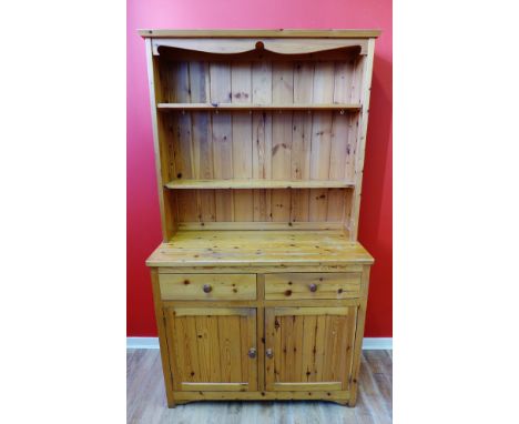 A pine two part kitchen cabinet having shelves to top above two short drawers and panel doored cabinets, raised on bracket fe