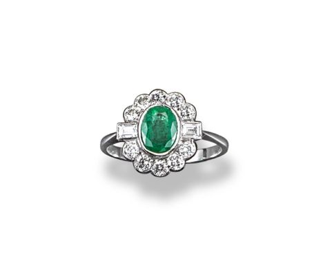 An emerald and diamond cluster ring, the oval shaped emerald is set within a surround of circular-cut and baguette-shaped dia