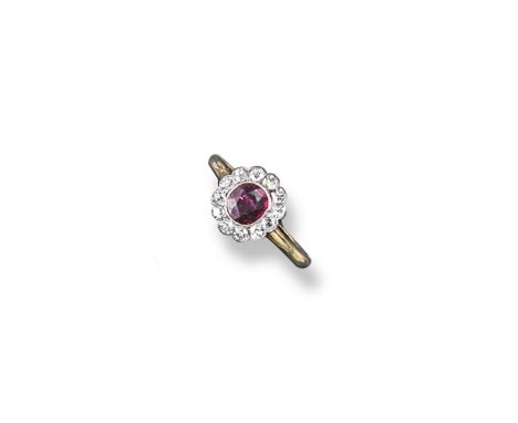 A ruby and diamond cluster ring, the oval shaped ruby is set within a surround of old circular cut diamonds in platinum and g